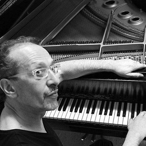 Black and white image of the pianist Hector Martignon sitting by a grand piano at the Roxy Bar