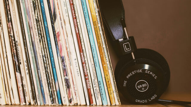 A row of vinyl records stacked on a shelf beside a pair of over-ear headphones resting against them.