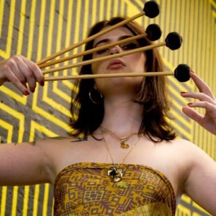 Vibraphonist Sasha Berliner holding mallets in front of her face.