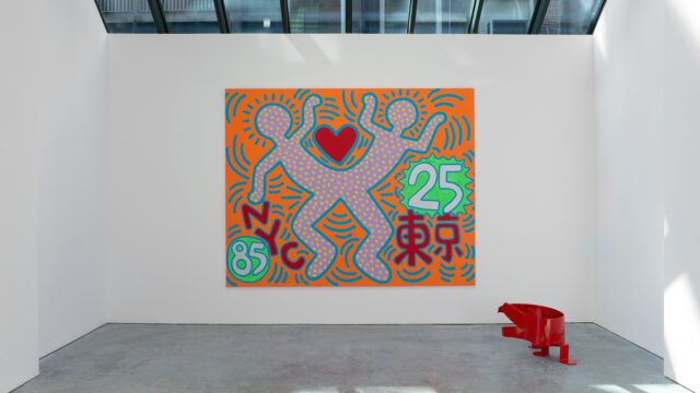 Gallery installation view of a large Keith Haring painting featuring a heart between two dotted figures.