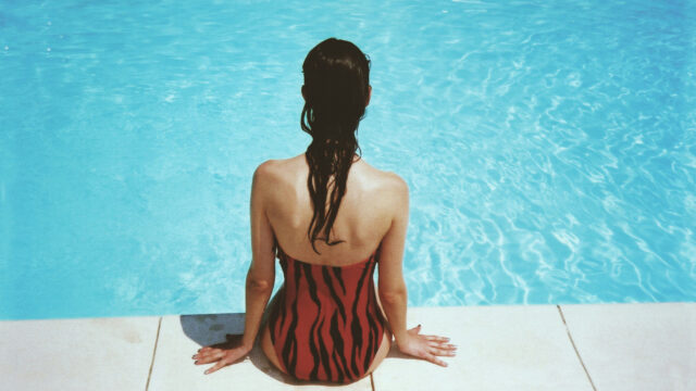 Woman in a tiger-print swimsuit sitting poolside, seen from behind.