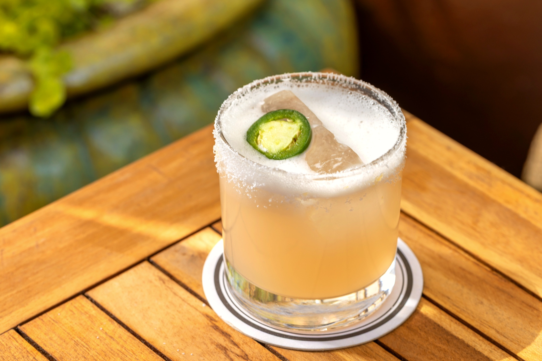 Summer cocktail with a frothy top and garnished with a jalapeño slice.