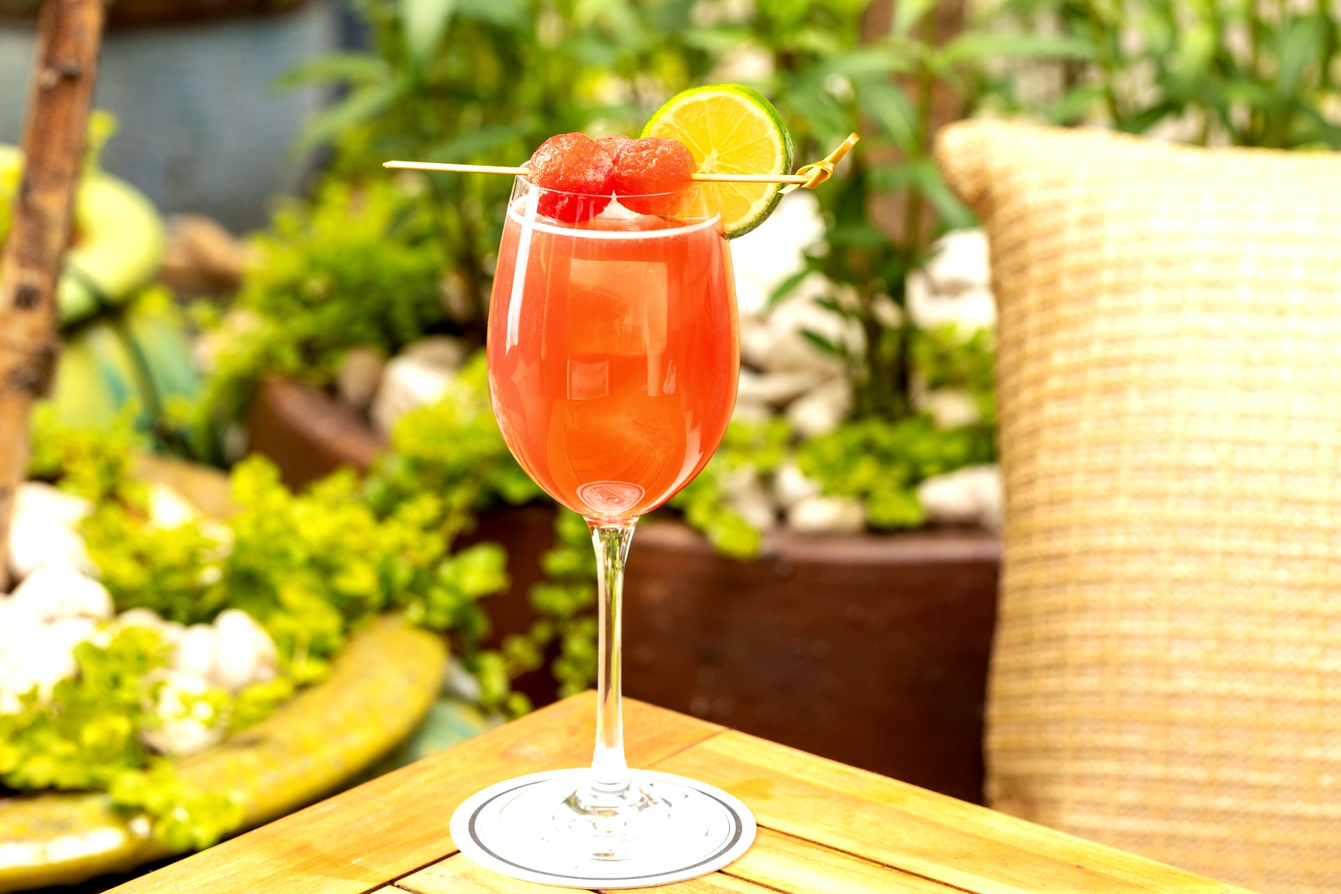 Red cocktail garnished with watermelon balls and lime.