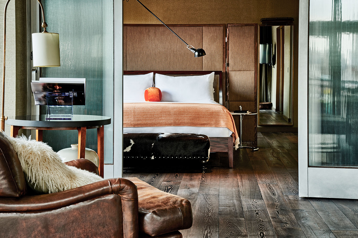 Loft North view of bedroom from the living room. A large bed with an orange throw blanket sites is surrounded by a leather headboard