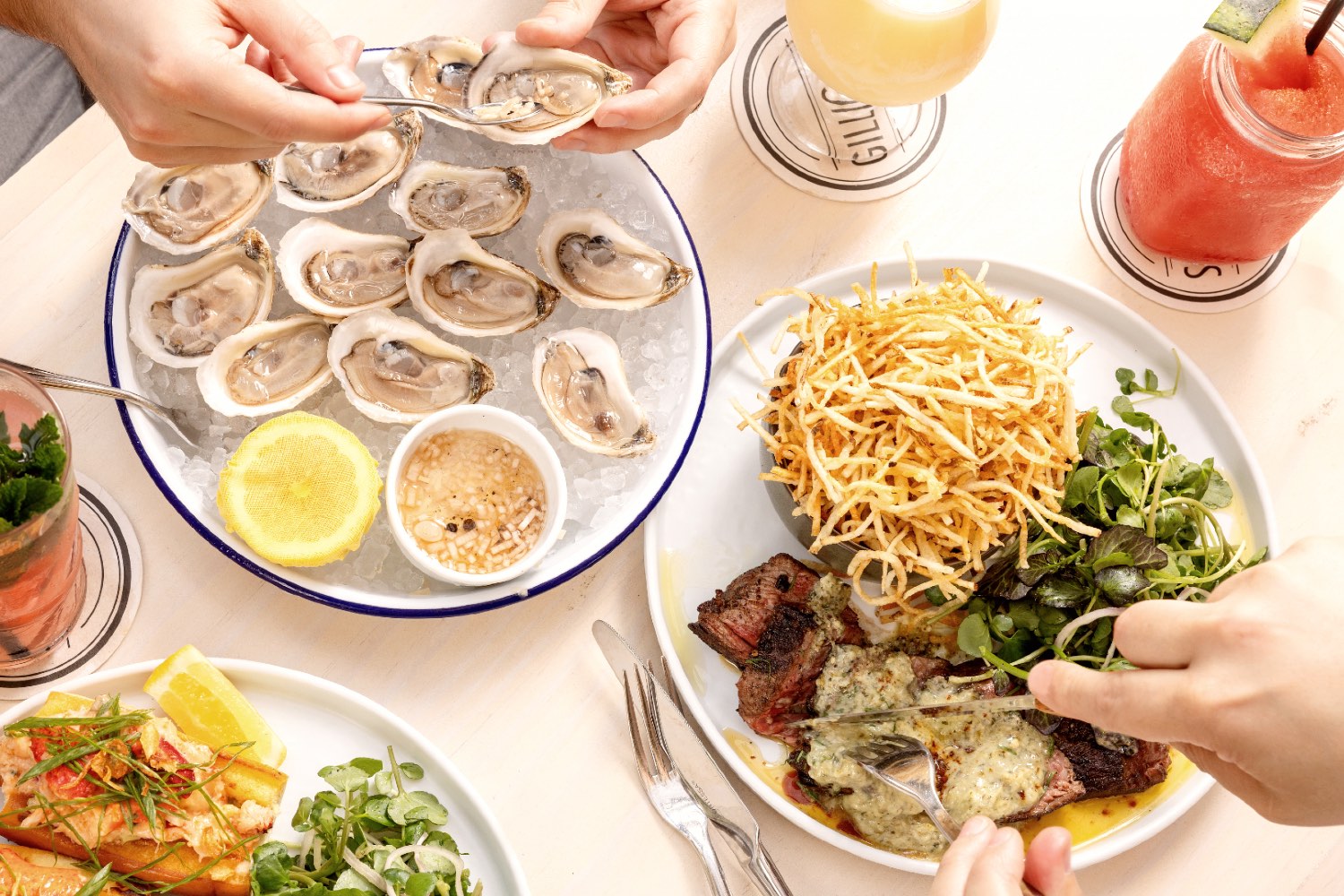 Table with Oysters, Steak Frites, a Lobster Roll and cocktails at Gilligan's in SoHo, NY.