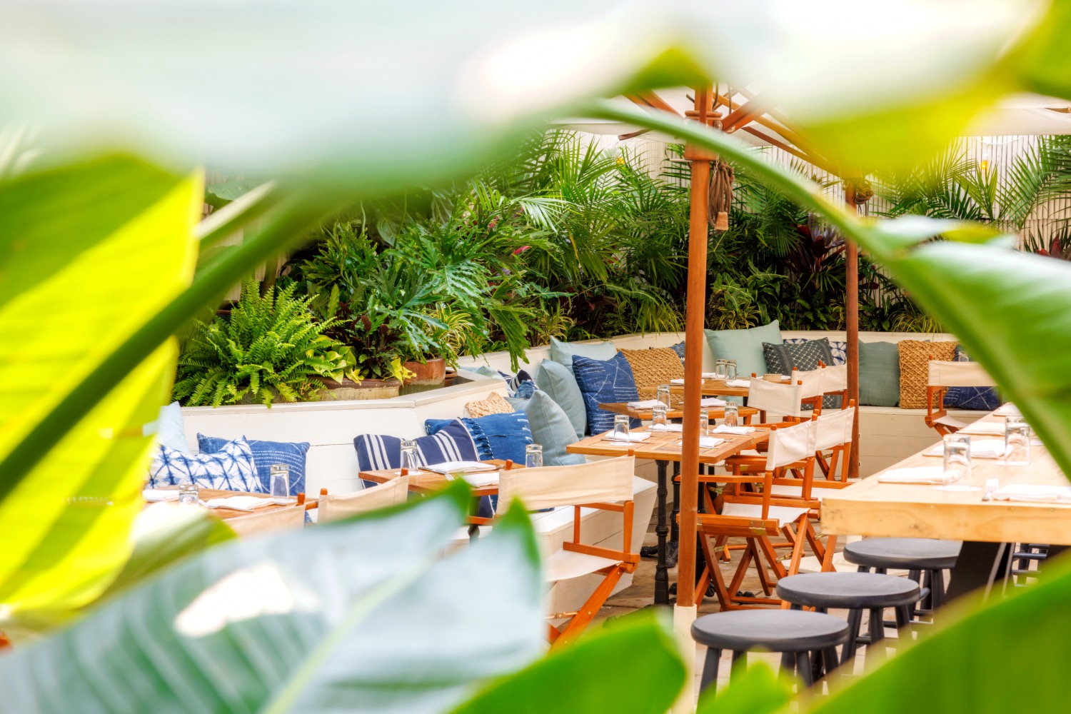 Table seating at Gilligan's outdoor restaurant as seen through lush green plants.