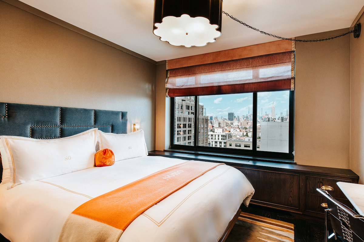 soho king bedroom with a king size bed with a orange throw blanket. There is a desk and a view of the Soho Neighborhood