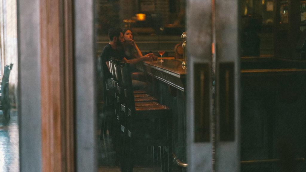 a couple sitting at bar. the viewer sees them through glass doors