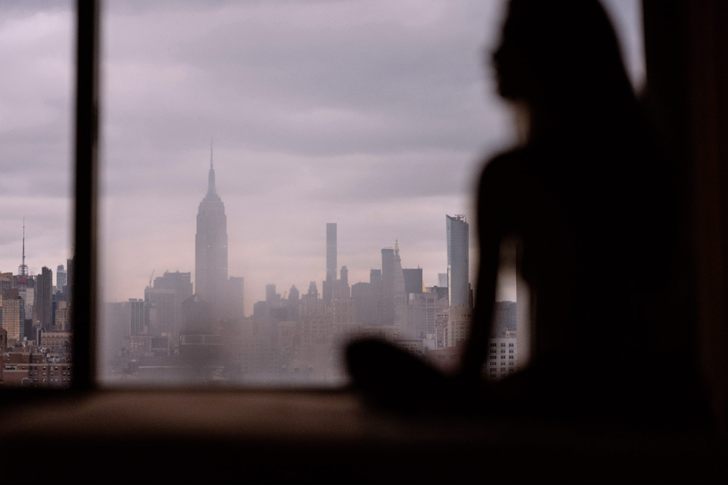 a silhouette of a woman meditating in front of a large window overlooking the midtown manhattan skyline