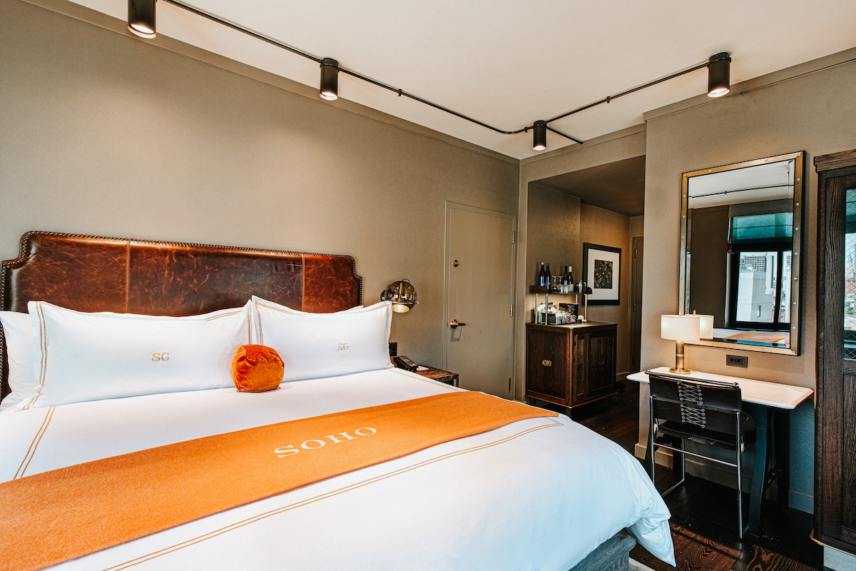 deluxe corner king bed with an orange throw blanker and a desk on the other side of the room