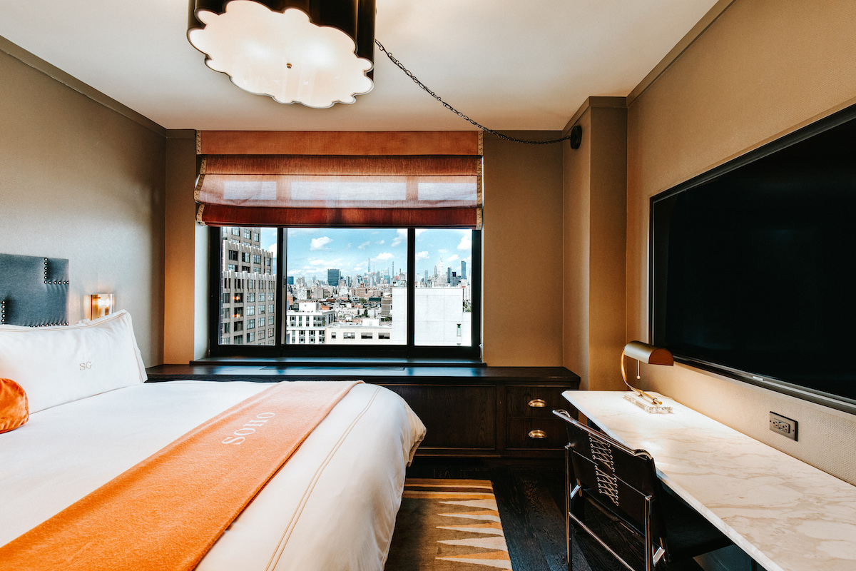 soho king bedroom with a king size bed with a orange throw blanket. There is a desk and a view of the Soho Neighborhood