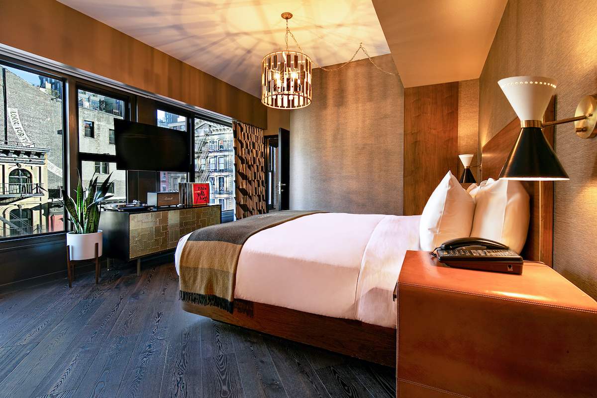 studio king bedroom with a king bed, side table and a tv with.a console. large windows span the wall