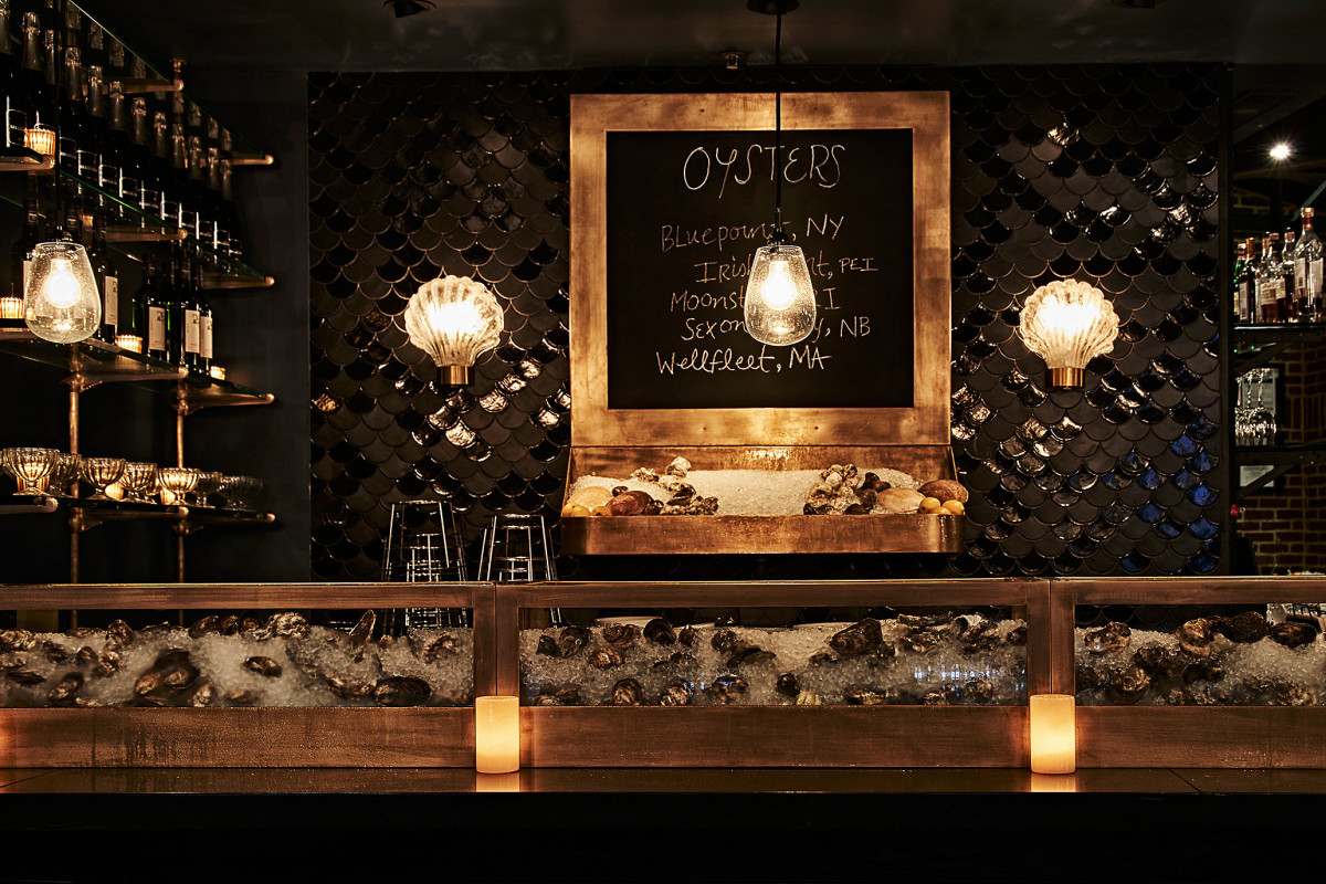 the oyster bar. there are shelves of liquor bottles, a menu board and oysters over ice on display