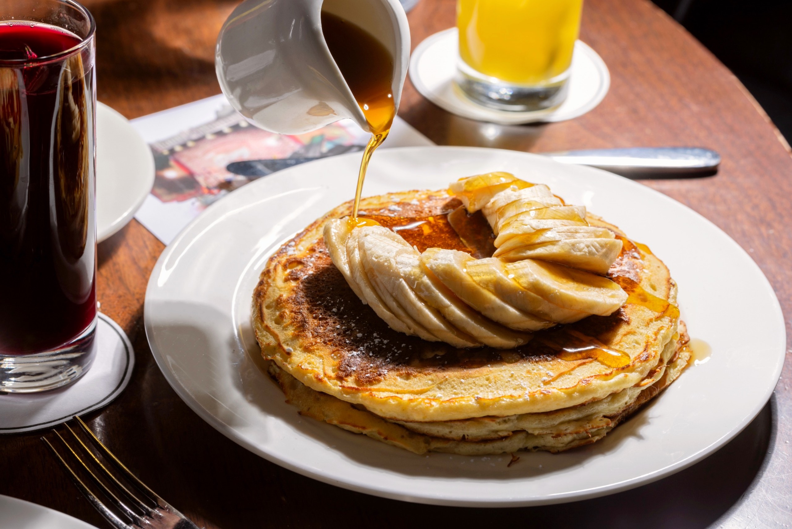 Syrup being poured over pancakes topped with chopped bananas.