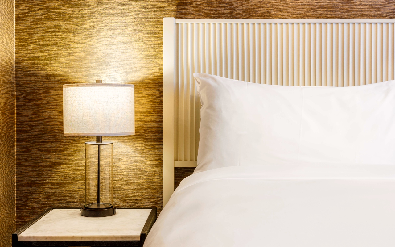 Closeup of pillow, headboard, and bedside table and lamp in a guest room at The Roxy Hotel.