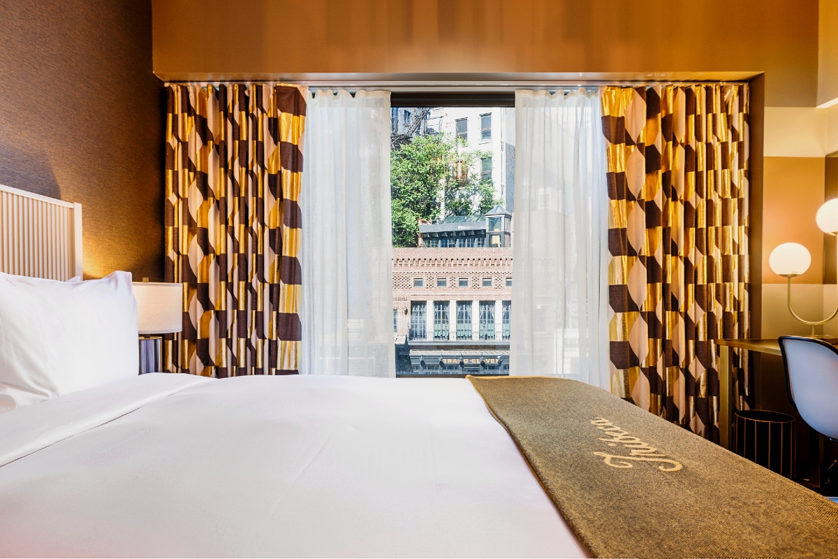 King bed with neighborhood view through the window of a Roxy Hotel guestroom.