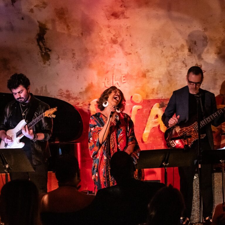 Woman singing onstage at the Django flanked by two guitarists on each side.