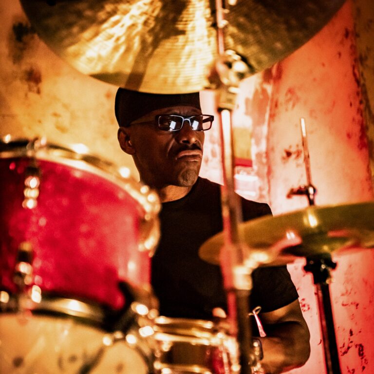 Closeup of a drummers face in between a cymbal and drum while on stage.