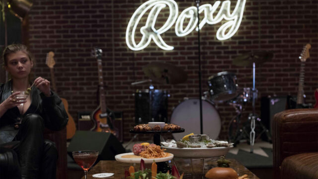 Roxy Bar Stage with instruments for live music and a neon lit Roxy sign.