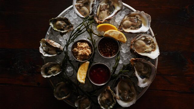 A detail shot of oysters on ice at Roxy Bar with three cups of sauce and lemon slices.