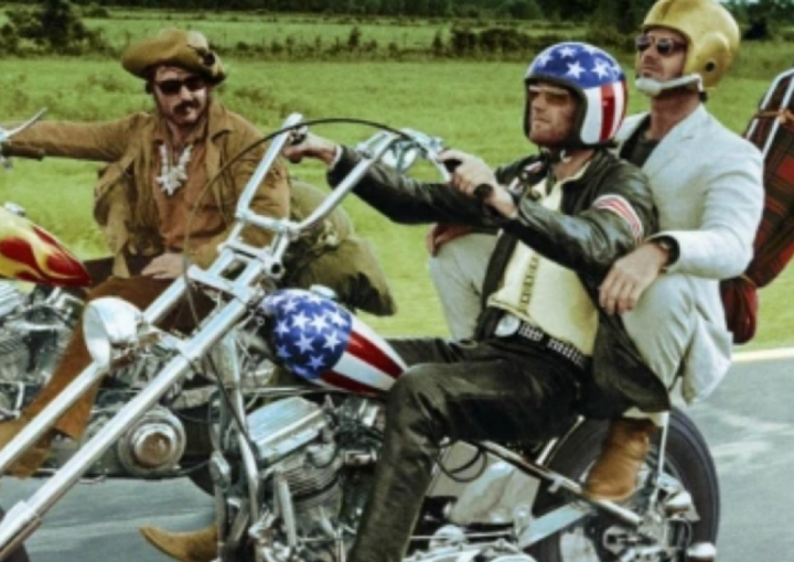 three men riding on motorcycles. one wears an american flag patterned helmet to match his bike and another is dressed as a cowboy