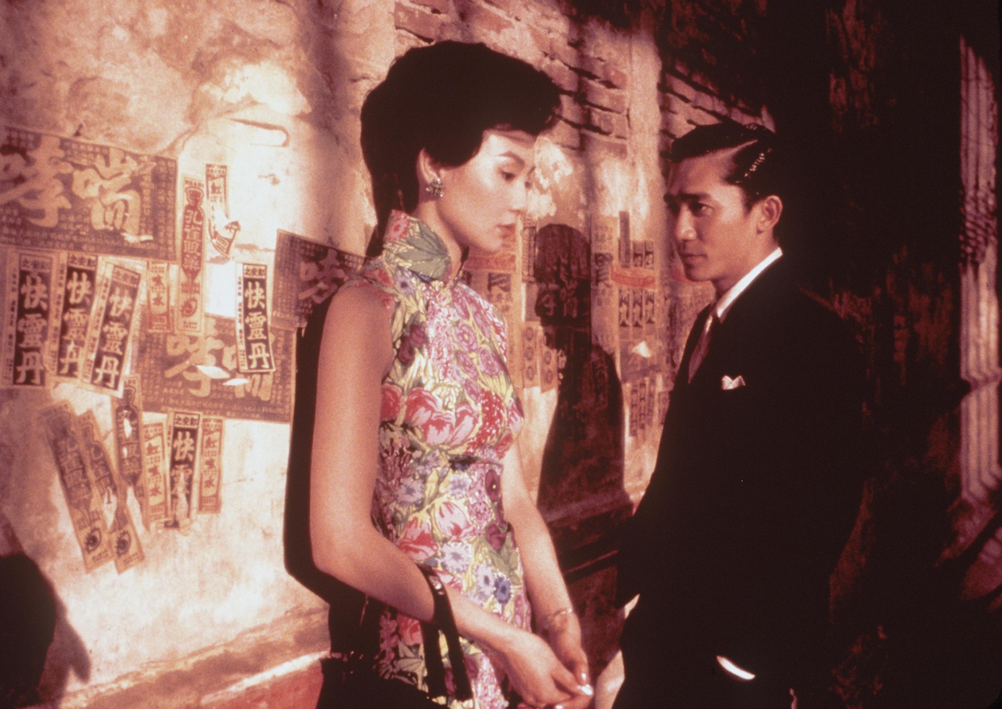 a man and a woman stand leaning against a wall. the woman looks down with the man stares at her longingly