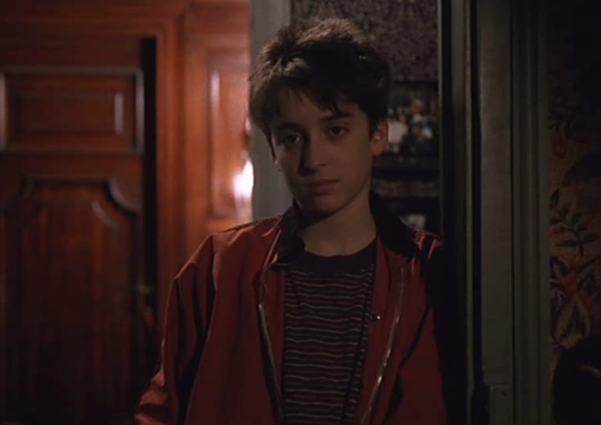 a young boy stands leaning against a door frame with an uninterested look on his face